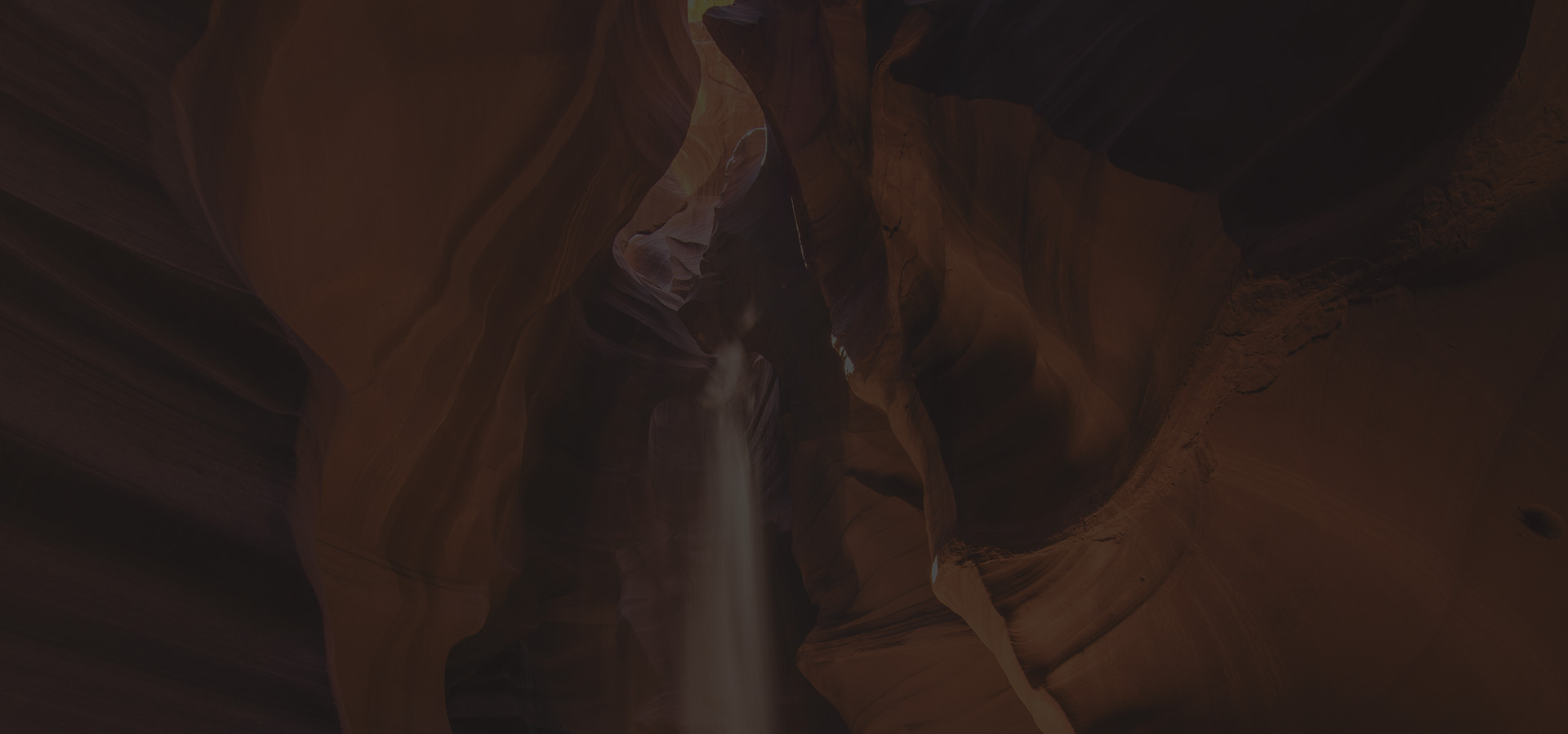 Dark, moody canyon interior with warm reddish sandstone walls and a shaft of light